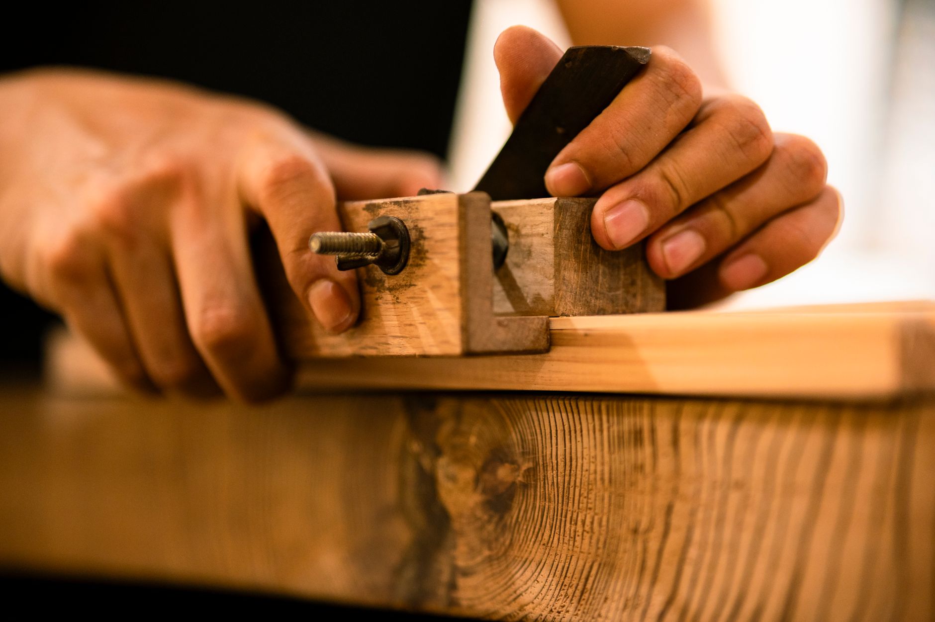 Hands using a chisel and wooden clamp to carve and shape a piece of wood.